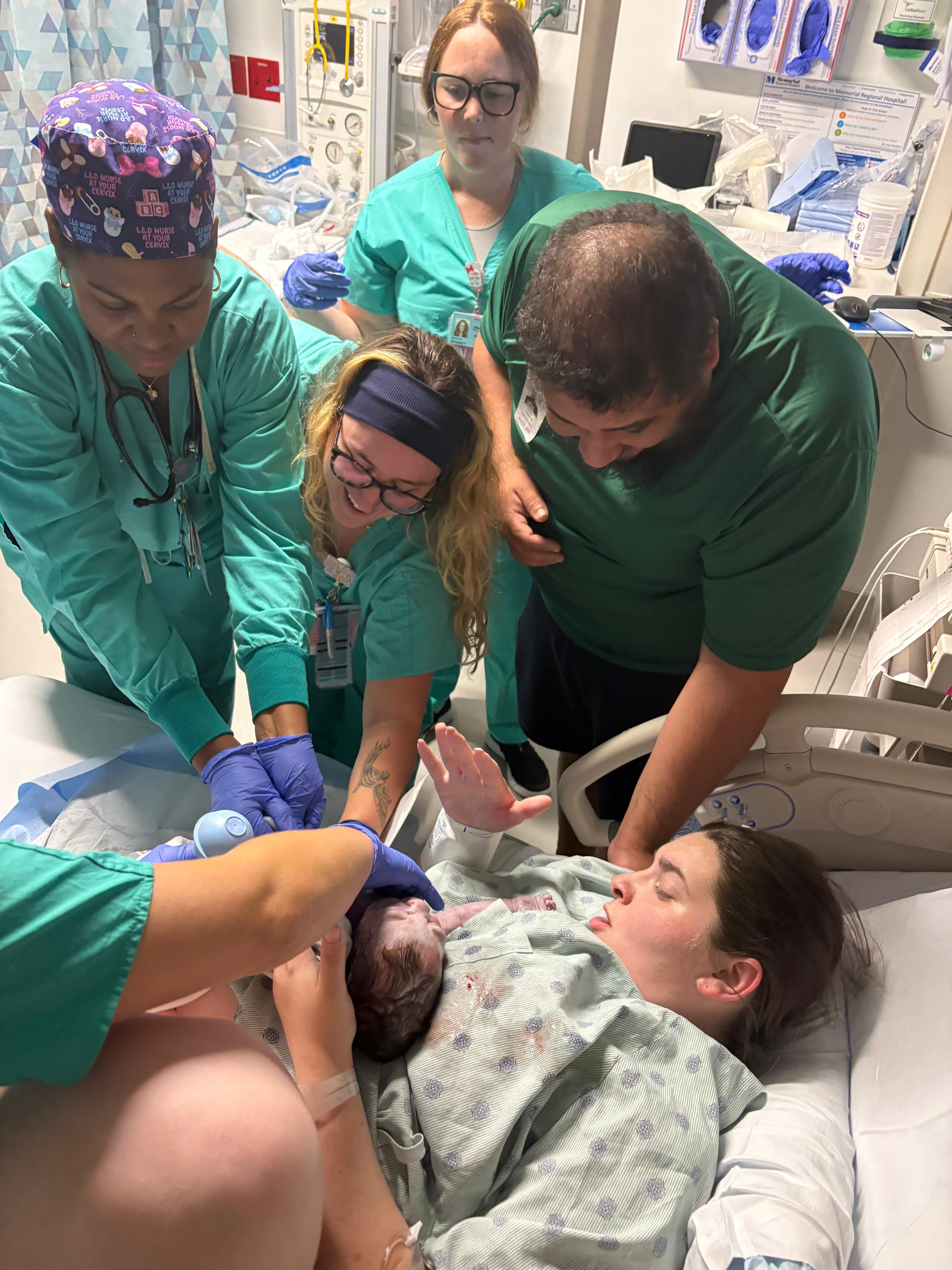 A care team gathered around a mother meeting her new baby
